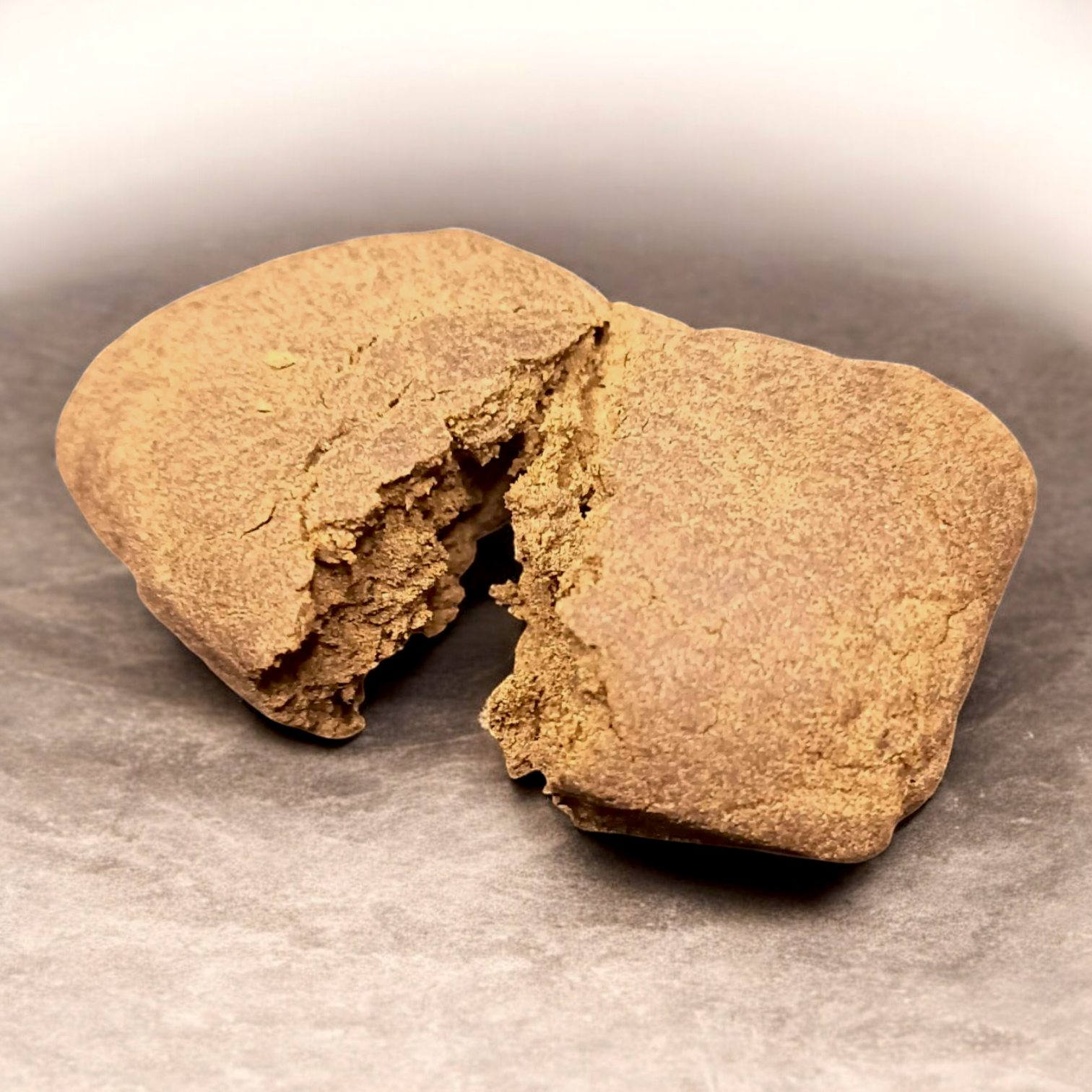 Bloc de résine de CBD brun clair, cassé en deux, montrant une texture compacte et friable sur fond neutre.