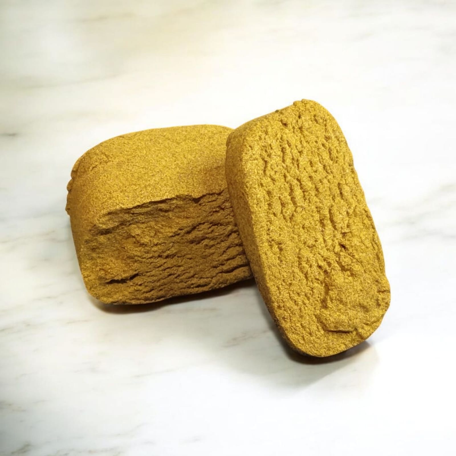 Bloc de résine de CBD jaune doré, coupé en deux, révélant une texture dense et friable, posé sur fond clair.